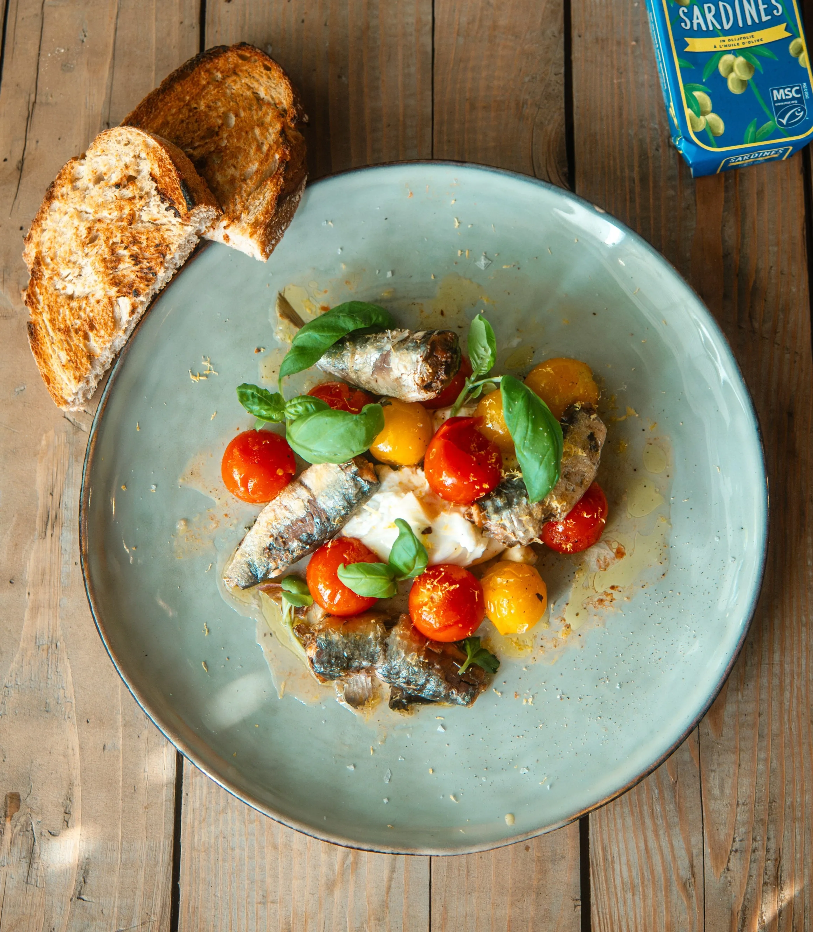 Sardine salad with cherry tomatoes, mozzarella, and basil on a blue plate with toast.